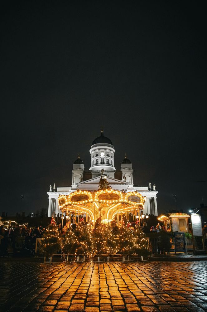 Der Dom von Helsinki bei Nacht, davor ein beleuchtetes Karussell und Lichterbäume auf dem Senatsplatz